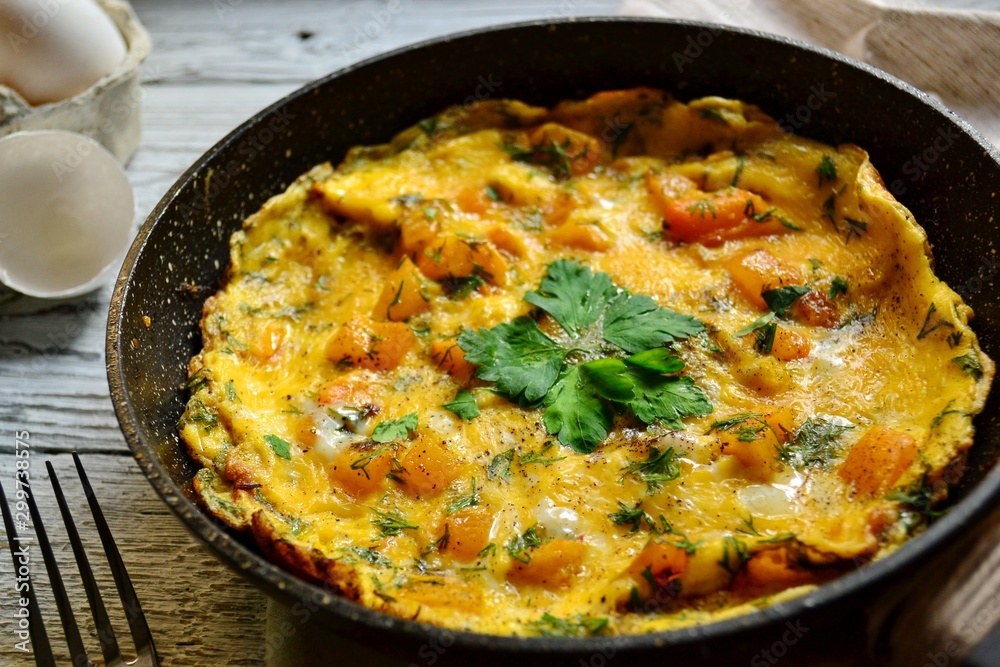 Appetizing omelet on a wooden light background. Omelet with yellow tomato, sweet yellow pepper and parsley leaves in a pan. Tasty breakfast. Appetizing omelet on a wooden light background. Omelet with yellow tomato, sweet yellow pepper and parsley leaves in a pan. Tasty breakfast.