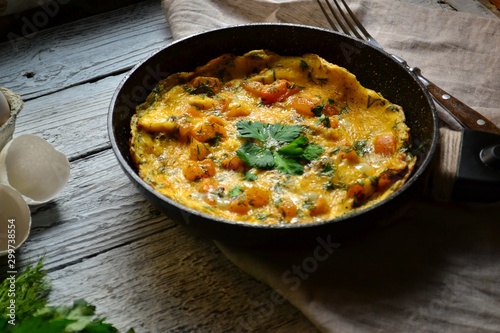Appetizing omelet on a wooden light background. Omelet with yellow tomato, sweet yellow pepper and parsley leaves in a pan. Tasty breakfast.