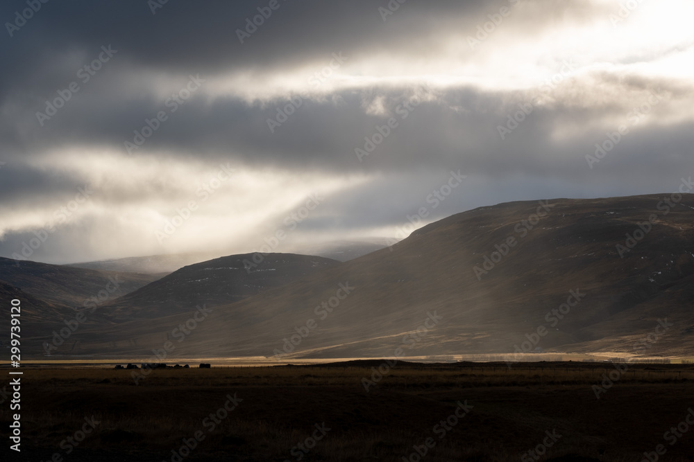 Sunlight penetrates through the clouds and illuminates a rain shower over the Svinadalur at Búðardalur in western Iceland.