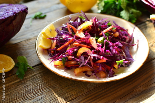Fresh spring salad with red cabbage, sweet pepper and carrots and parsley. Salad with cabbage in a beautiful plate. Wood background. Sunlight. Top view. Delicious healthy food made from vegetables.