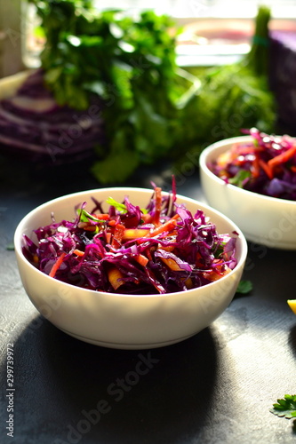 Fresh spring salad with red cabbage, sweet pepper, carrots and parsley leaves. Salad with cabbage in a white bowl. Dark black concrete background on the table. Sunlight. Top view. healthy food