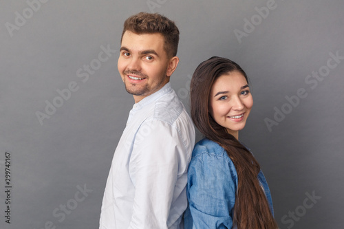 Relationship Concept. Young couple studio standing back to back isolated on grey smiling positive to camera