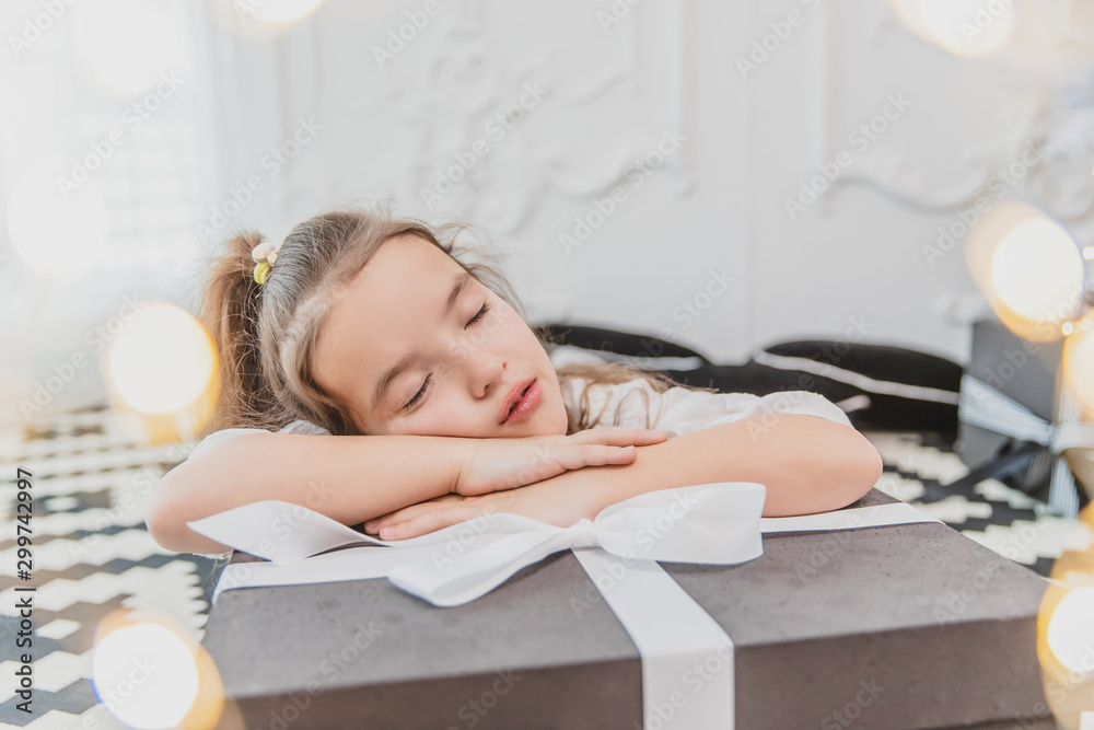 Sweet girl with ponytail is sleeping on big Christmas present, looking amazing.