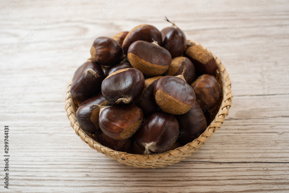 Obraz premium top view of chestnuts in a wicker basket on a wooden table
