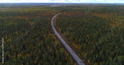 Cars on a forest road, Aerial, drone shot, following lots of old vintage vehicles, driving between foliage color trees , on a partly sunny, fall day, in Pyha-Luosto national park, Sodankyla, Finland photo