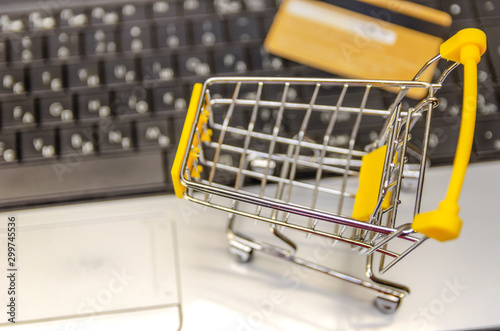 laptop with a small yellow shopping cart and a credit card close-up. The concept of online shopping