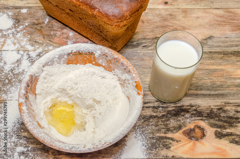 Fresh bread brick on the table closeup. Next is a bowl of flour and egg, a glass of milk. Fresh bread brick on the table closeup. Next is a bowl of flour and egg, a glass of milk.