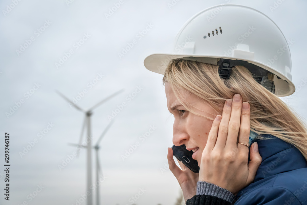 girl engineer in a helmet talking on a mobile phone on the background of wind generators in cloudy weather girl engineer in a helmet talking on a mobile phone on the background of wind generators in cloudy weather