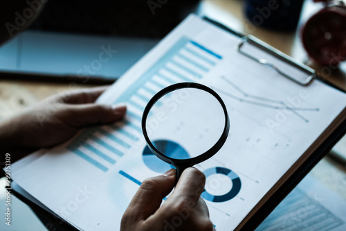 Businessman looking through a magnifying glass to documents. Business assessment and audit. Magnifying glass on a financial report. Concept of search.