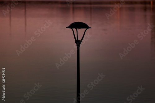 Black lantern with a spiderweb on the embankment of Vistula in Krakow. Early morning beautiful light paints reflections in the water