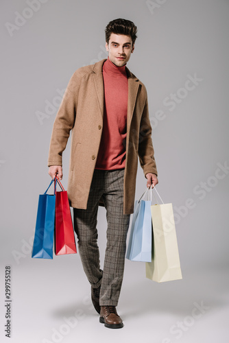 stylish man in beige coat holding shopping bags on grey