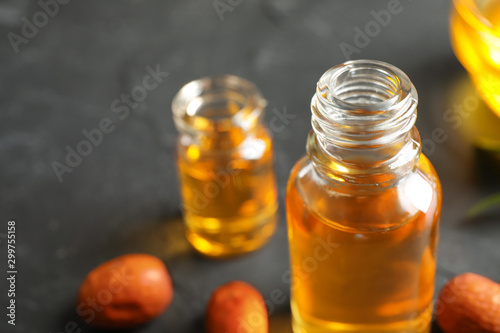 Jojoba oil in glass bottle on table, closeup view