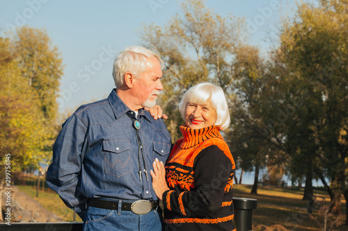 Happy elderly man and woman sitting on a bench in autumn day. Relaxed senior couple sitting on a park bench. Grandfather gently kisses grandmother on the forehead. photo