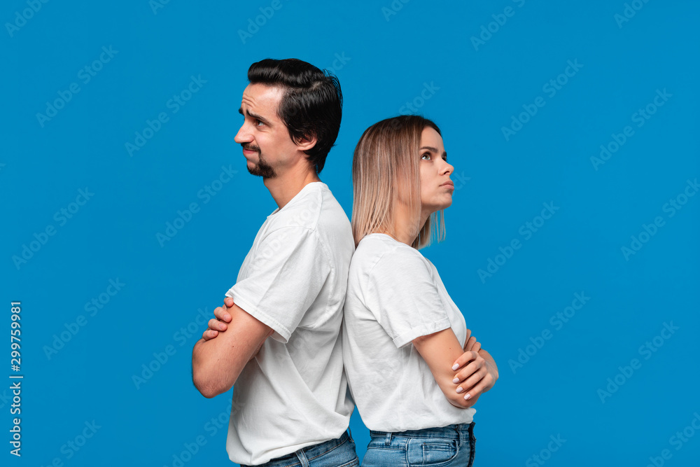 Upset couple of a young blond woman and brunet bearded man with mustaches in white t-shirts and blue jeans posing isolated over blue background. Upset couple of a young blond woman and brunet bearded man with mustaches in white t-shirts and blue jeans posing isolated over blue background.