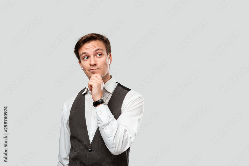 Thoughtful young businessman in a white shirt and grey vest holding hand close to chin. Concept of idea and thinking. Thoughtful young businessman in a white shirt and grey vest holding hand close to chin. Concept of idea and thinking.