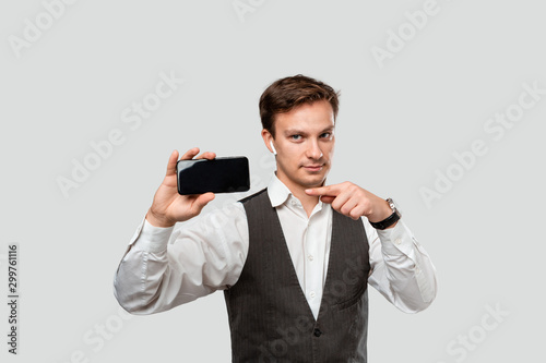 Handsome businessman in a white shirt and grey vest showing screen of a smartphone.