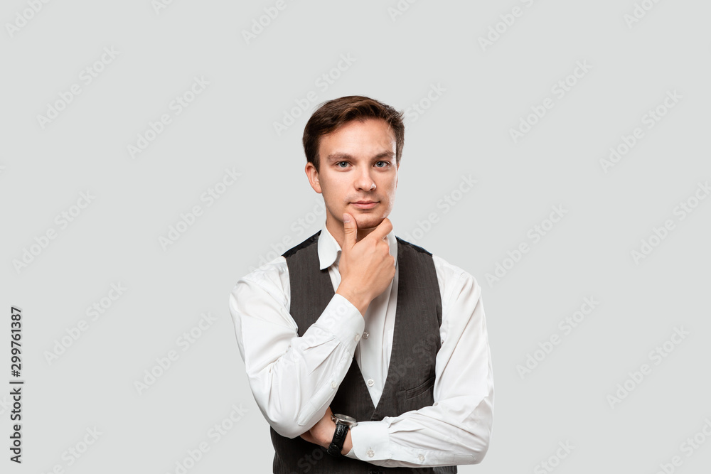 © ianachyrva - Thoughtful young businessman in a white shirt and grey vest holding hand close to chin. Concept of idea and thinking.