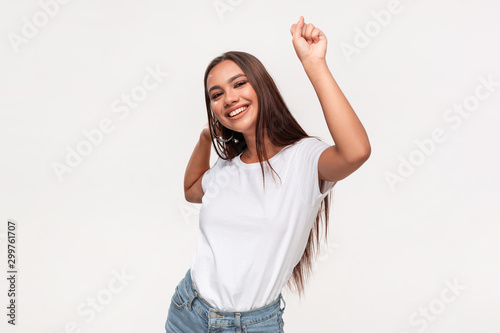 Beautiful african-american teenager in a white t-shirt and blue jeans dancing isolated over white background.