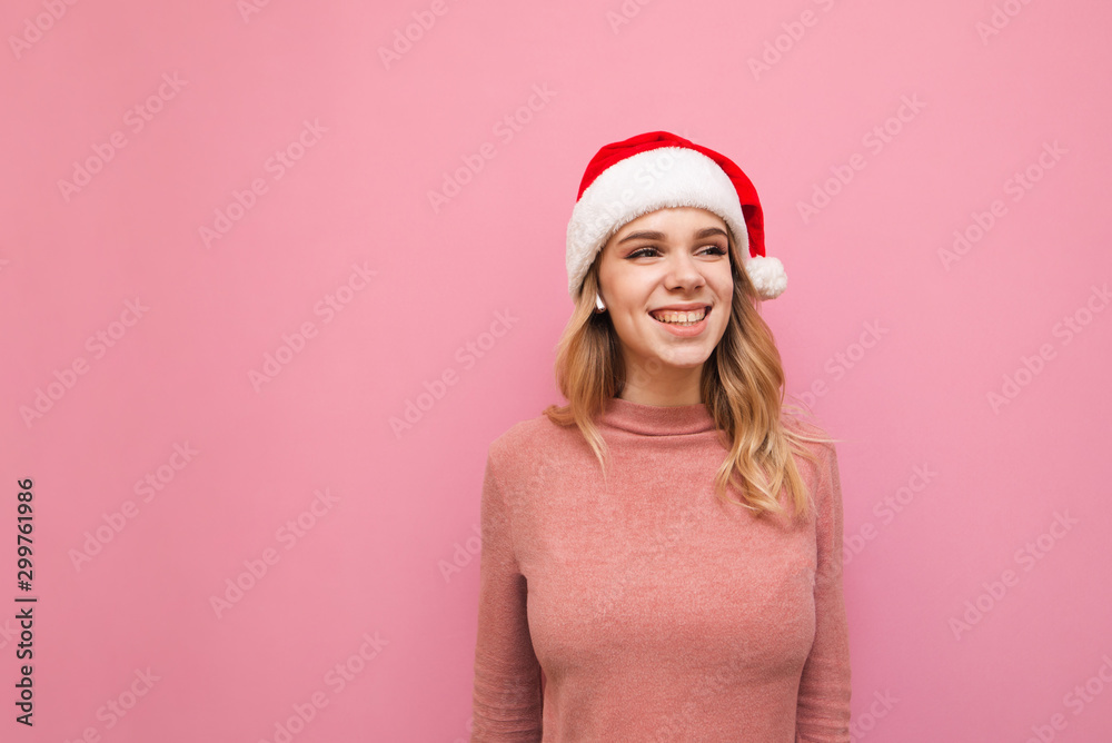 Smiling cute girl in Christmas hat and pink clothes isolated on pink, looking away and rejoicing.Happy lady in a Christmas hat stands on a pink background and listens to music in wireless headphones Smiling cute girl in Christmas hat and pink clothes isolated on pink, looking away and rejoicing.Happy lady in a Christmas hat stands on a pink background and listens to music in wireless headphones