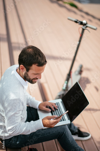 Young businessman outdoors using phone and laptop