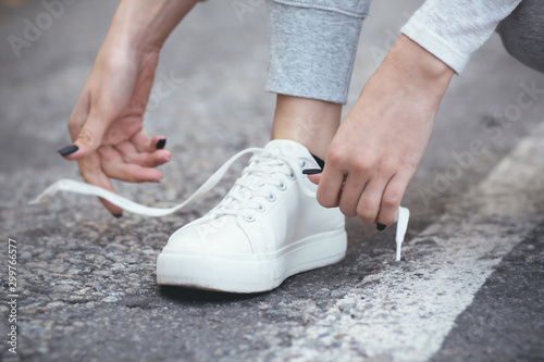 girl squatted down to tie shoelaces on white sneakers on asphalt road, autumn sport concept outdoors
