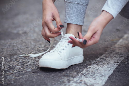 girl squatted down to tie shoelaces on white sneakers on asphalt road, autumn sport concept outdoors