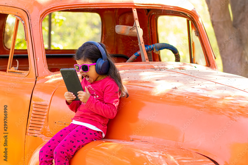 Naklejka premium Little girl listening to music on the tablet with her headphones in the truck car