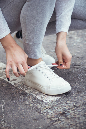 girl squatted down to tie shoelaces on white sneakers on asphalt road  autumn sport concept outdoors