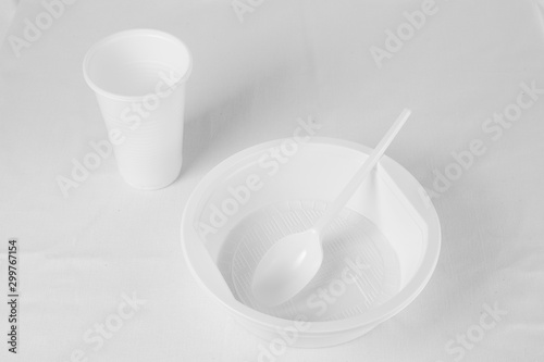 White disposable plastic plate, spoon and glass on a white background. White key.