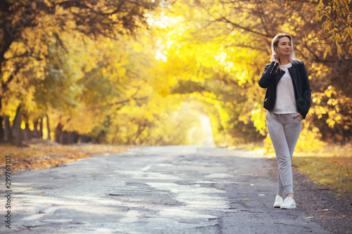 young woman in casual sportswear with a backpack standing on the asphalt road of a suburban road  girl travels walking and enjoying the autumn nature
