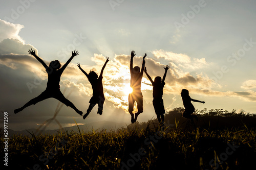 Silhouette group of happy children jumping playing on mountain at sunset, sum...