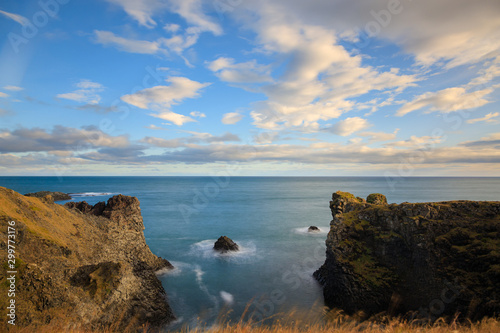 West coast sea cliffs of Snaefellsnes Peninsula on Iceland in long exposure photo. Pure blue water with high cliffs above sea. Beautiful colourful scenic view of basalt rock reef..