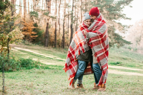 Couple huggings travelers covered with plaid in the forest. Concept of trekking, adventure and seasonal vacation. © zadorozhna