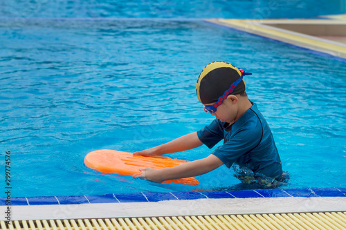 5 years old Lonely boy warm up with orange swimming kickboard before learning to swim in the blue swimming pools.