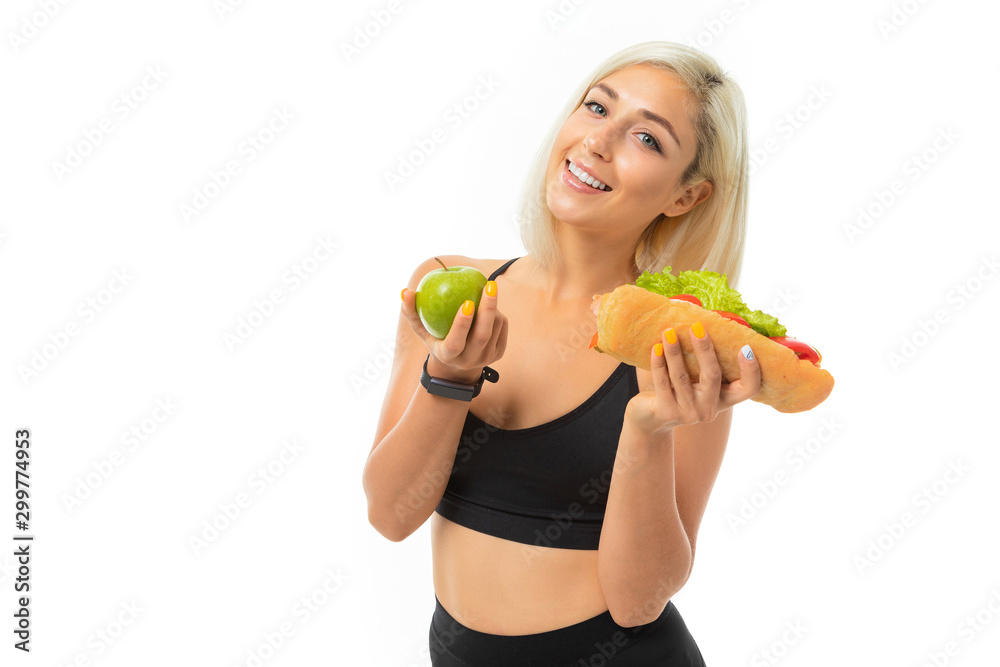 A young sports girl with blonde hair in a black sports top and black leggings holds a green apple and sandwich A young sports girl with blonde hair in a black sports top and black leggings holds a green apple and sandwich