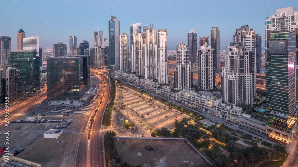 Panorama of Business bay with big parking in Dubai from night to day transition timelapse. Aerial view with towers and skyscrapers with moving long shadows. Traffic on the road with sunrise. Panorama of Business bay with big parking in Dubai from night to day transition timelapse. Aerial view with towers and skyscrapers with moving long shadows. Traffic on the road with sunrise.