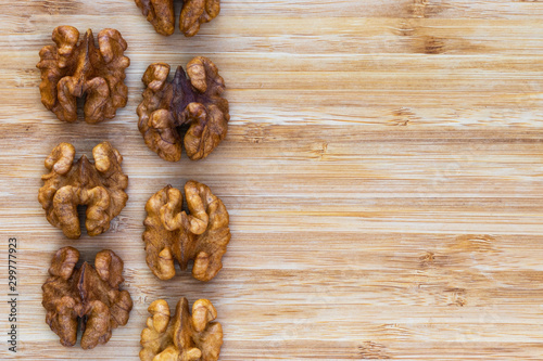 Walnuts lie in two rows on a brown wooden background on the left, on the right - an empty place, top view