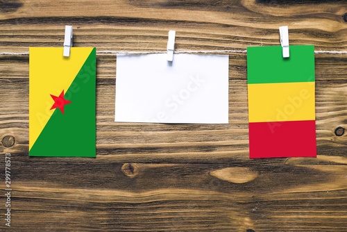 Hanging flags of French Guiana and Mali attached to rope with clothes pins with copy space on white note paper on wooden background.Diplomatic relations between countries.