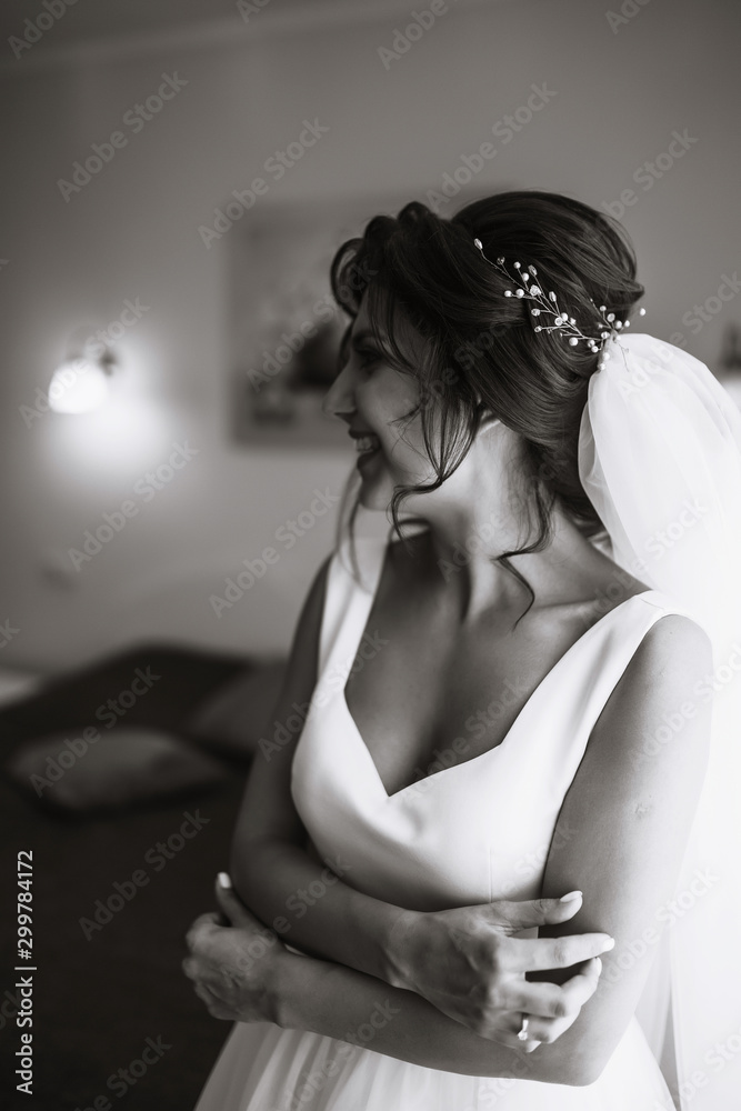 Naklejka premium Morning of the bride. Beautiful smiling brunette bride in a white dress with a wedding bouquet in her hands. Elegant woman with professional make up and hair style. Wedding morning of the bride. 