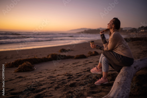 Woman enjoying hot drink on a sunset near ocean