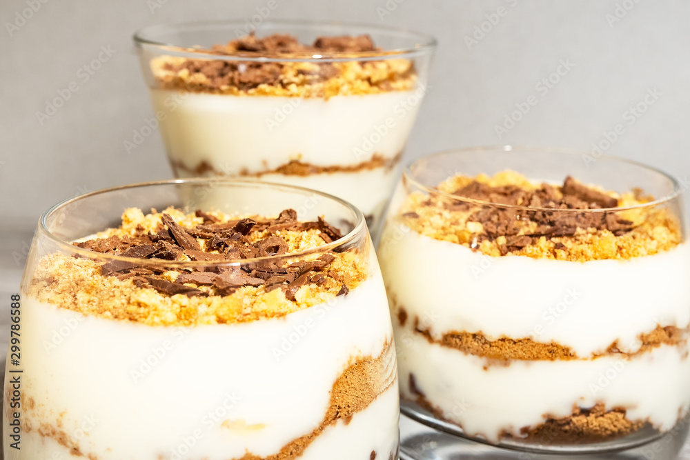 Classic tiramisu dessert in a glass on a gray wooden background. Brightly lit chocolate cake in the amount of three pieces.