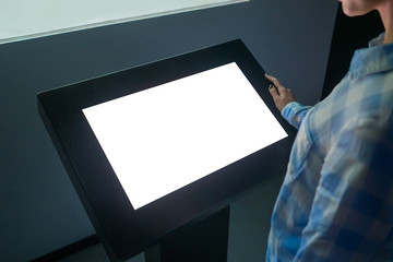 Woman looking at white blank interactive touchscreen display of electronic multimedia kiosk in dark room of technology exhibition - close up view. Mock up, copyspace, template and futuristic concept