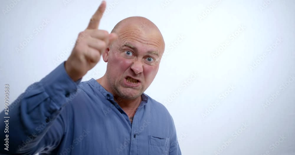 A close-up portrait of an angry, scary bald middle-aged man in a blue shirt, he is in the Studio on a white background, pointing his finger at us, yelling, swearing, wrinkling his forehead, staring A close-up portrait of an angry, scary bald middle-aged man in a blue shirt, he is in the Studio on a white background, pointing his finger at us, yelling, swearing, wrinkling his forehead, staring