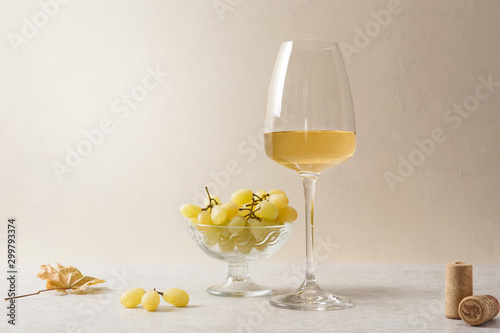 A glass of white wine, grapes and corks on the table.