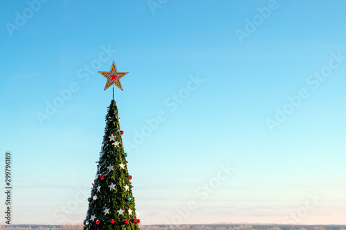 Christmas tree. Festive New Year mood. The crown of a large spruce with a star and toys against a blue cloudless sky. Copy space.