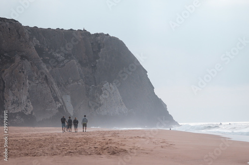 Beach with a big cliff in background in a winter day with four people walking. Paria Grande Sintra Portugal