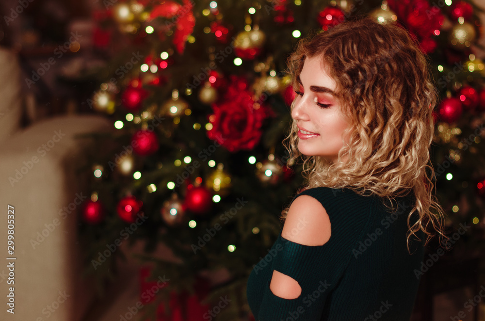 Christmas. Beautiful smiling woman. Manicure nails. Makeup. Healthy long hair style. Elegant lady in green dress over christmas tree lights background. happy new year.