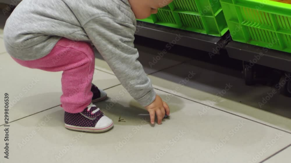 Handheld shot of adorable little toddler picking plum from floor at supermarket, smiling and trying to eat it Handheld shot of adorable little toddler picking plum from floor at supermarket, smiling and trying to eat it