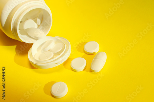 Scattered pills over yellow background. White bottle and white  pills on yellow background.  Health and medicine concept.