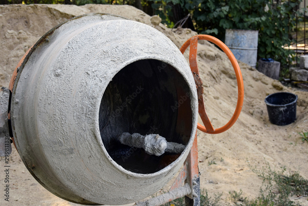 Electric concrete mixer on the background of a heap of sand. Construction machinery at the production site. Electric concrete mixer on the background of a heap of sand. Construction machinery at the production site.